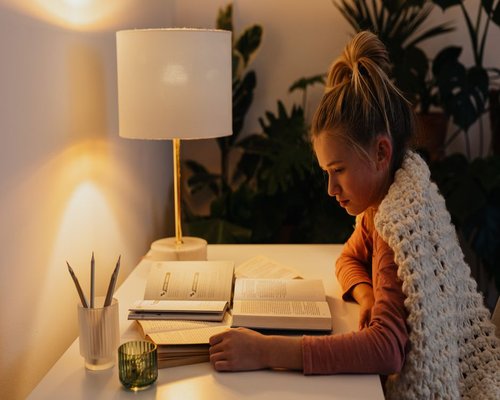 Person reading a book with a warm reading lamp nearby
